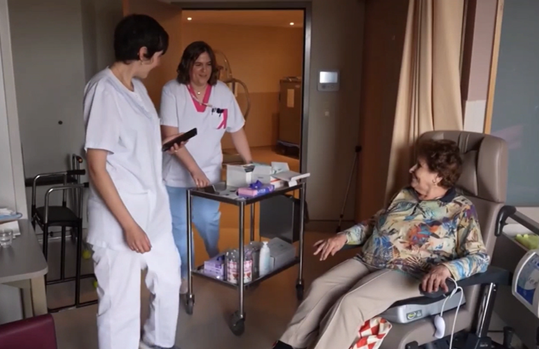 Soignants en EHPAD entrant dans la chambre d’une résidente avec un chariot de soins bucco-dentaires pour réaliser un examen bucco-dentaire visuel.